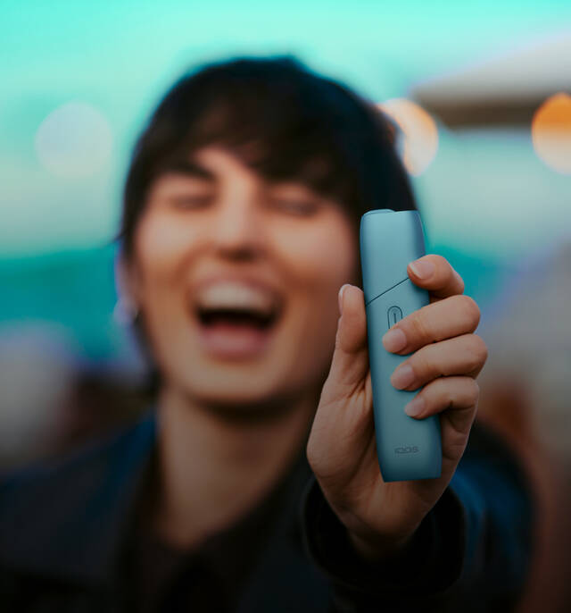 Woman laughing and holding IQOS Originals One heated tobacco device in turquoise color.