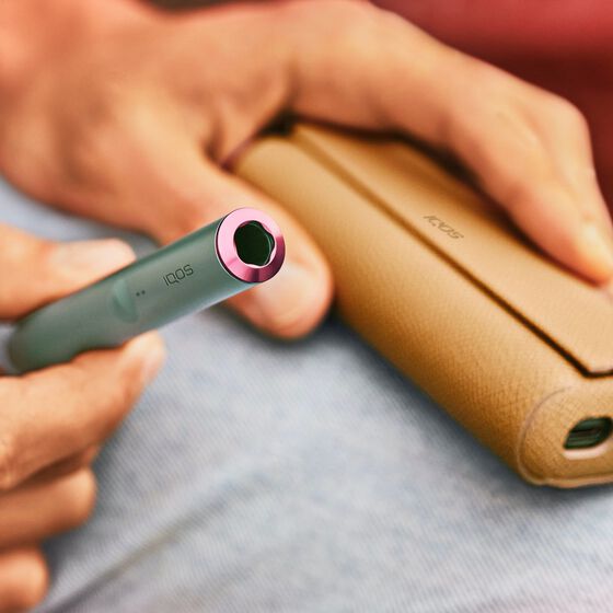 A Jade Green IQOS ILUMA Holder with a ring accessory held by a person with a leather-like full wrap.