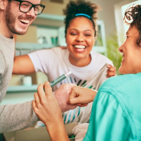 A man holding an IQOS device fist bumps his friend; a smiling woman looks on.