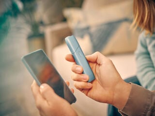 Hands holding a mobile phone and IQOS Originals One device, logging into myIqos to get the most of the heated tobacco device.