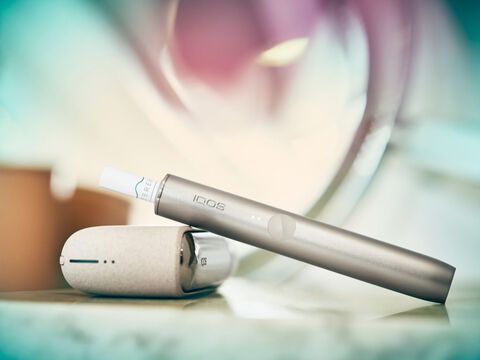 A Jade Green IQOS ILUMA Holder with a ring accessory held by a person with a leather-like full wrap.