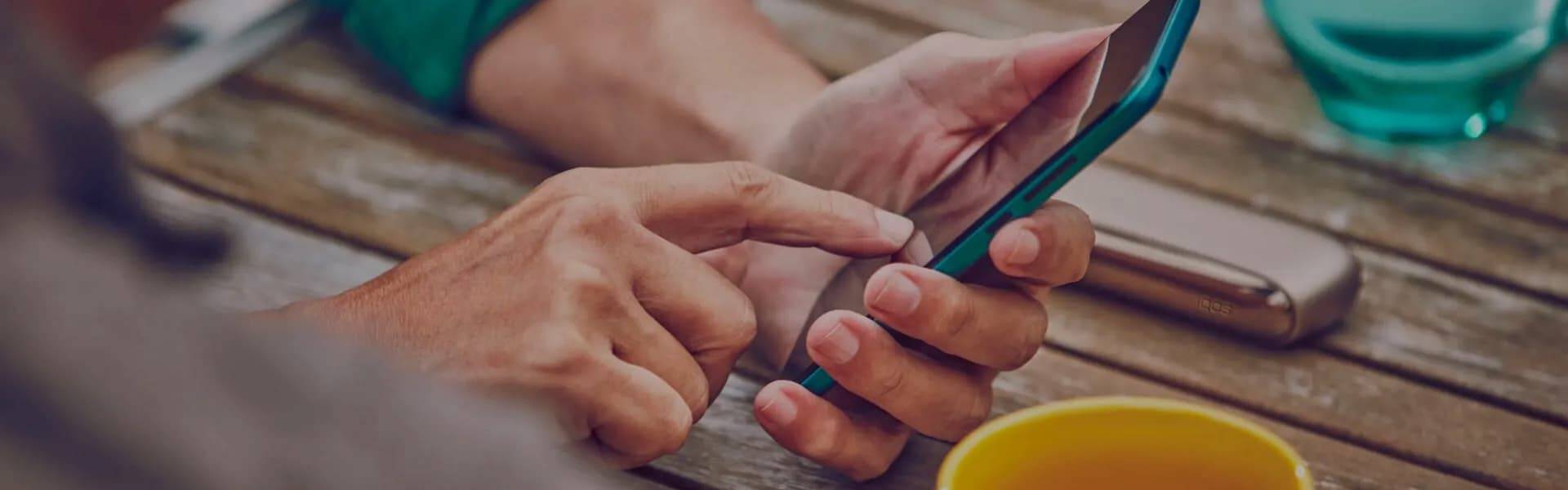 Man checking his phone with the IQOS device on the table