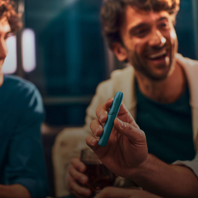 Men laughing and holding IQOS Originals Duo holder in turquoise color.
