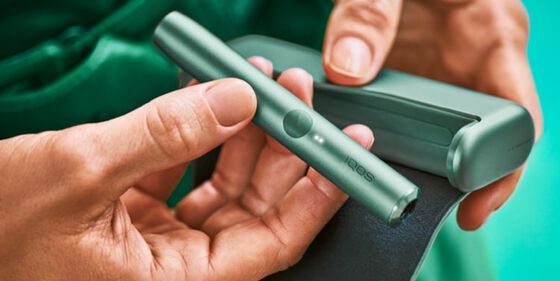 A person placing an IQOS ILUMA Pocket Charger into a charging station.