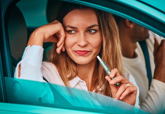 A woman uses an IQOS ILUMA device while sitting in a car.
