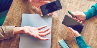 Hands holding smartphones and one IQOS device.