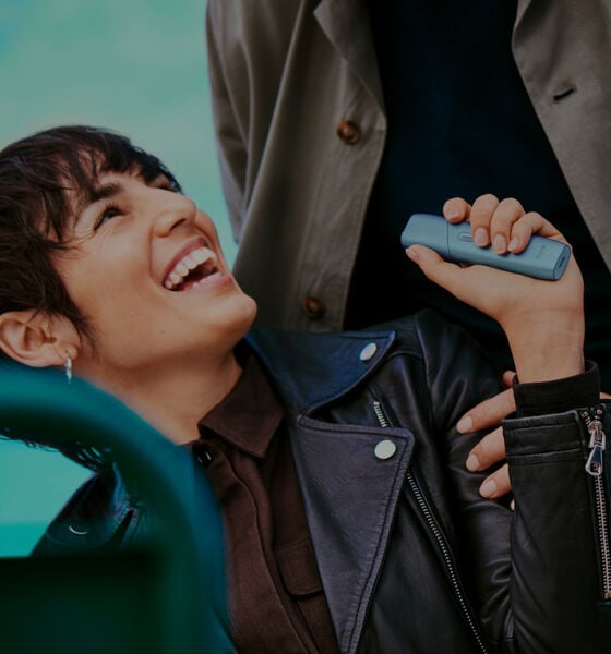 Smiling person holding IQOS Originals Duo holder in red color.