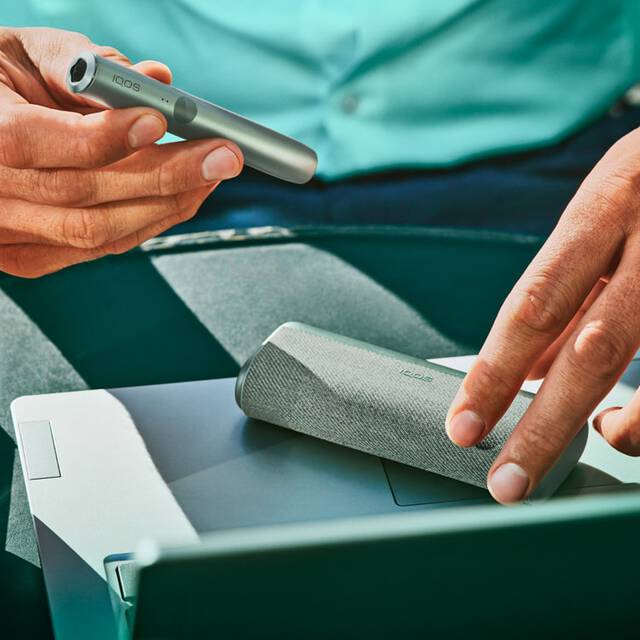 A man's hands opening a [colour] IQOS ILUMA device.