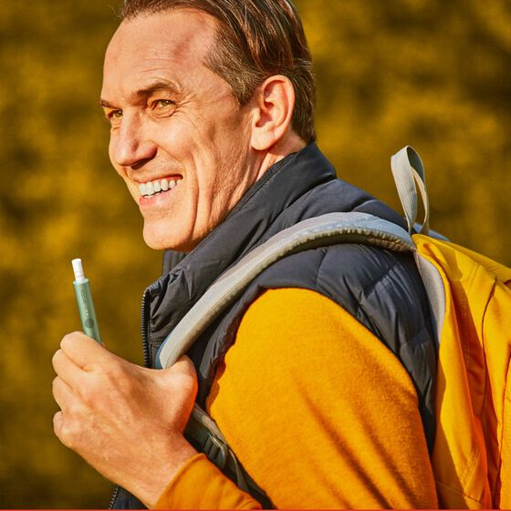 A man with a rucksack holds an IQOS device.