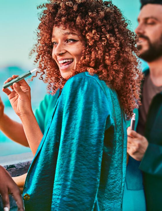 A group of friends, one woman holding a Jade Green IQOS ILUMA Holder.