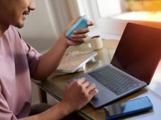 Man holding IQOS originals Duo device and typing on laptop.