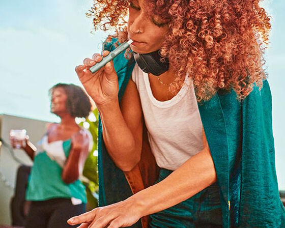 A woman with curly hair holding an IQOS device.